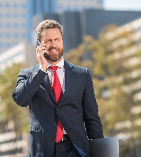 cheerful successful businessman in suit talking on phone standing outdoor, mobile technology.