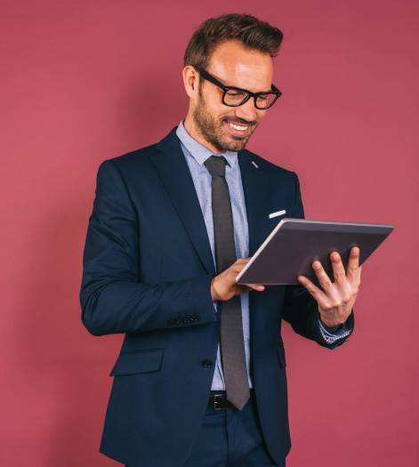 Confident handsome happy businessman in a suit working in a tablet on red background